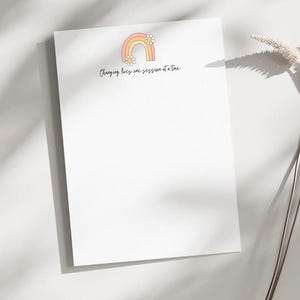 Puede incluir: Bloc de notas blanco con un arcoíris rosa y naranja con flores blancas y el texto "Cambiando vidas una sesión a la vez".