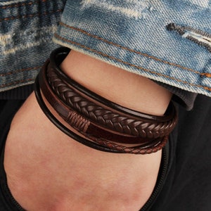 May include: A multi-layered bracelet set featuring various brown leather bands. The set includes braided, smooth, and wrapped leather designs. The bracelets are in shades of dark and medium brown, creating a stylish accessory.