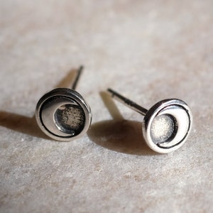 May include: A pair of silver crescent moon stud earrings. The earrings are small and delicate, with a simple design.