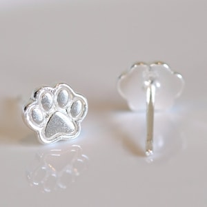 May include: A pair of silver paw print stud earrings. The earrings are small and delicate, and they would make a great gift for any dog lover.