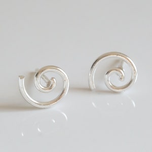 May include: A pair of silver-colored stud earrings. Each earring features a spiral design, resembling a curled shape. The earrings are set against a white background, highlighting their minimalist and modern aesthetic. These earrings are perfect for everyday wear.