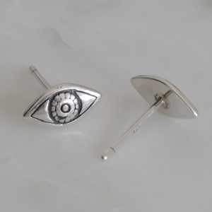 May include: A pair of silver earrings with a detailed eye design. The earrings are in the shape of an almond and have a post back.
