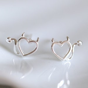 May include: A pair of silver earrings with a heart shape and devil horns. The earrings are small and delicate.