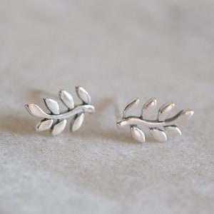 May include: A pair of silver earrings featuring a delicate branch design with small leaves. The earrings are simple and elegant, perfect for everyday wear.