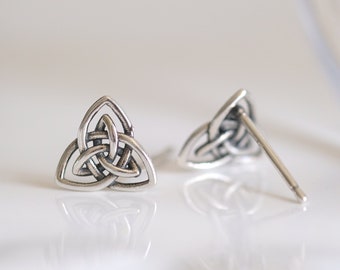 May include: A pair of silver-colored stud earrings featuring a Celtic knot design. The earrings are in the shape of a triangle with interwoven lines, and the posts are visible. The earrings are displayed on a white surface.