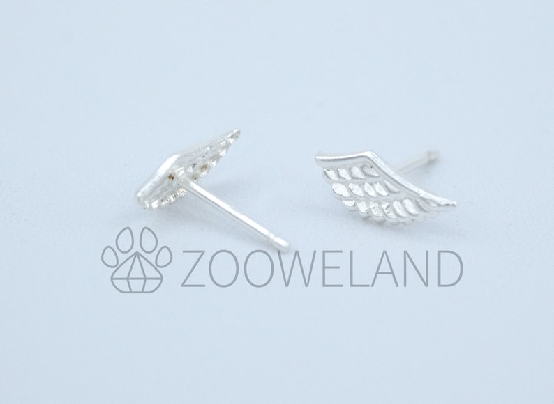 May include: A pair of silver wing-shaped stud earrings. The earrings feature feather-like detailing and a post for insertion. The image includes the text "ZOOWELAND" in grey.