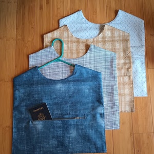 Può includere: Quattro sacche per abiti in tessuto con diversi motivi. La borsa superiore è blu chiaro con un motivo bianco. La seconda borsa è marrone con un motivo a quadri bianchi. La terza borsa è grigia con un motivo a quadri bianchi. La borsa inferiore è blu con un motivo bianco e una tasca con cerniera. Un passaporto è nella tasca.