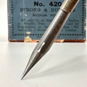 May include: A silver metal pen nib with the text "No. 420 EX FI LONDON" engraved on the side. The nib is pointed and sharp, ready for writing.