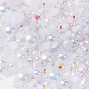 May include: A close-up of a variety of white and iridescent pearl and crystal beads. The beads are scattered on a white surface.