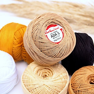 May include: Six balls of yarn in various colours, including white, beige, brown, and yellow. The label on one ball reads "Ariadna Col. 0404 ADA 5 40 tex x 6 50g/205m".