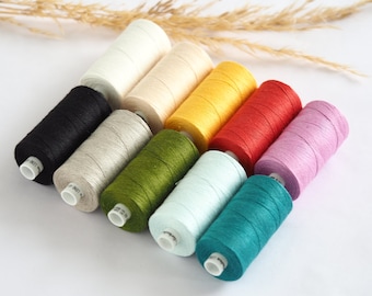 May include: A set of ten spools of thread in various colors, including black, white, beige, yellow, red, pink, green, and blue. The spools are arranged in a semi-circle on a white surface.