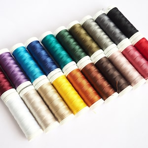 May include: A collection of spools of thread in various colours, including red, orange, yellow, green, blue, purple, brown, and grey. The spools are arranged in a row, with the colours gradually transitioning from one to the next.