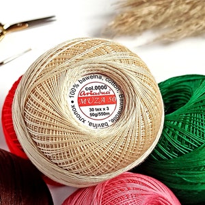 以下が含まれることがあります： ベージュの糸の玉のクローズアップ。ラベルには「100% bawełna, cotton, Baumwolle. Ariadna MUZA 50 col.0000 30 tex x 3 50g/550m bavlna, хлопок」と書いてあります。