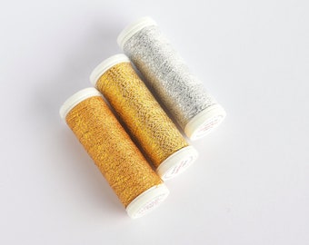 May include: Three spools of metallic thread in gold, silver, and a darker gold color. The spools are wrapped in white paper with red lettering.