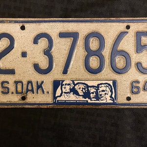 May include: A vintage South Dakota license plate with the number 2-37865 and the year 64. The plate features a blue border and a small image of Mount Rushmore.