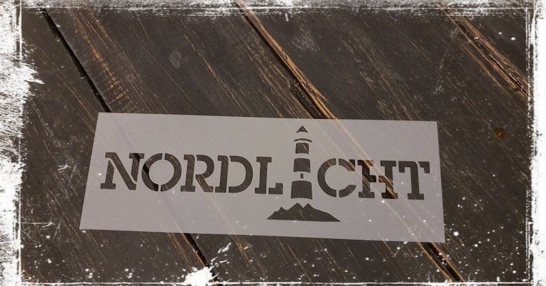 Puede incluir: Una plantilla blanca con la palabra "NORDLICHT" y un gr&aacute;fico de faro. La plantilla est&aacute; sobre una superficie de madera marr&oacute;n oscura.