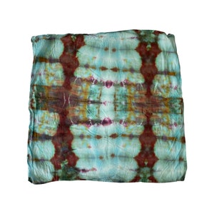 Puede incluir: Una bufanda cuadrada de tela teñida anudada con un patrón simétrico de colores marrón, verde y azul.