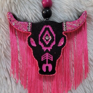 May include: Black and pink glitter bull skull with pink fringe hanging from the bottom.