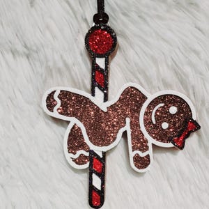 May include: A gingerbread man Christmas ornament with a glittery brown body and white icing details. The ornament is hanging from a black string and is attached to a red and white striped candy cane.