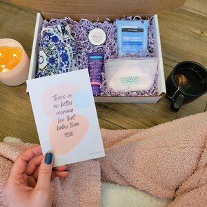 May include: A gift box filled with items for new mothers, including a card that reads "There is no better momma for that baby than you." The box contains a small blue and white patterned bag, a small jar of cream, a tube of nipple cream, a package of makeup remover wipes, and a package of breast pads.