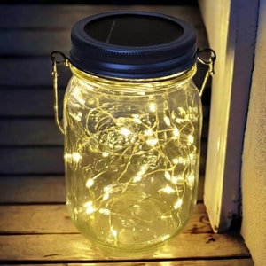 May include: A glass jar with a black lid and a metal handle, filled with white fairy lights. The jar is sitting on a wooden surface.