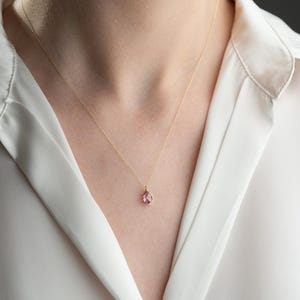 Puede incluir: Un delicado collar de cadena de oro con un pequeño colgante de piedra preciosa rosa en forma de lágrima.