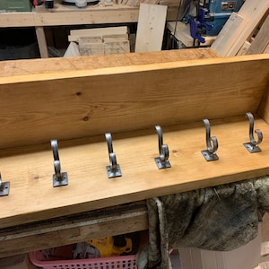 May include: A wooden shelf with a backboard and six metal hooks. The shelf is stained a light brown colour and the hooks are a silver colour.