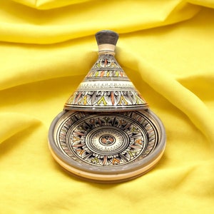 May include: A ceramic tagine with a white base and a conical lid. The lid and base are decorated with intricate geometric patterns in shades of orange, green, and black.