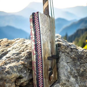 May include: A wooden musical instrument with a decorative fabric trim. The instrument is made of wood and has a string attached to it. The instrument is sitting on a rock.