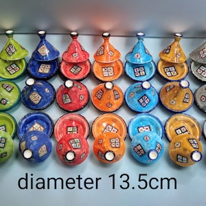 Puede incluir: Una colección de 18 tajines de cerámica coloridos con diseños intrincados. Los tajines están dispuestos en filas y tienen un diámetro de 13,5 cm. El texto "diámetro 13,5 cm" está escrito debajo de los tajines.