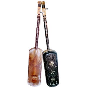 May include: Two traditional stringed instruments. One is light brown with a rectangular body and a long neck. The other is black with white floral inlay and a similar shape. Both have tuning pegs at the top.