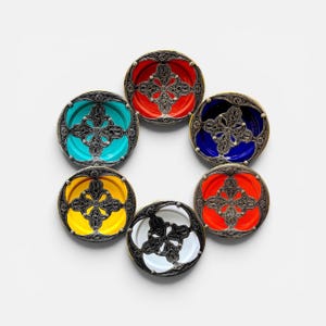 May include: A collection of six small, round dishes with ornate silver-colored filigree borders. Each dish features a different vibrant color in the center: red, blue, orange, yellow, turquoise, and black and white. The dishes are arranged in a circular pattern.