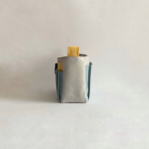 May include: A gray and blue fabric organizer with a yellow handle. The organizer has multiple pockets and compartments.