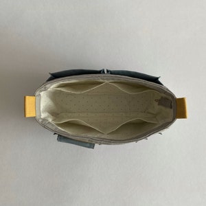 May include: A gray fabric organizer with multiple compartments and yellow handles. The organizer is empty and has a white dotted lining.