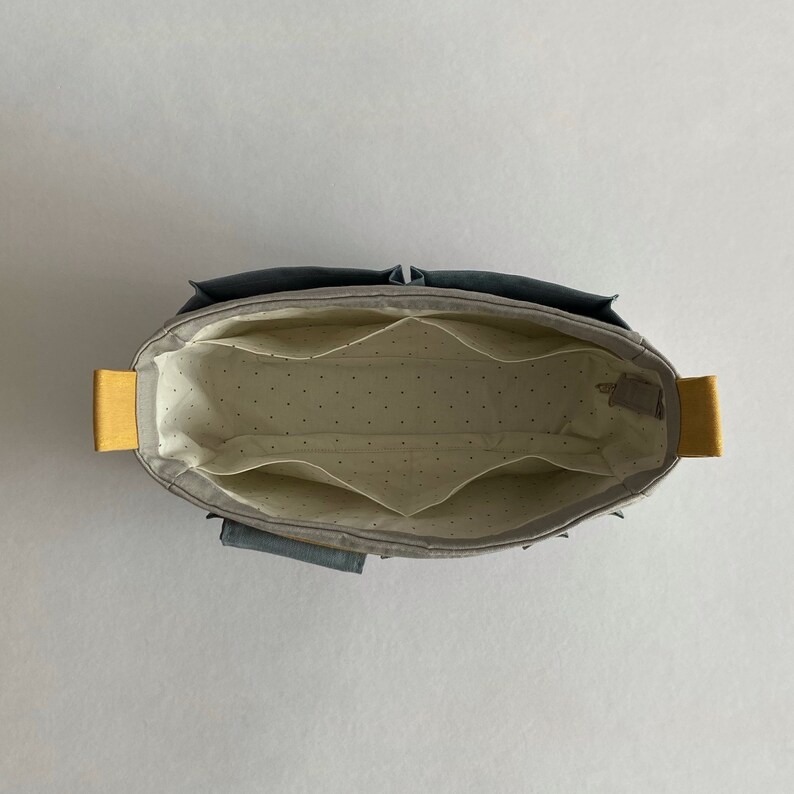 May include: A gray fabric organizer with multiple compartments and yellow handles. The organizer is empty and has a white dotted lining.