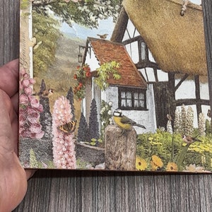 May include: A cottage with a thatched roof and white walls, surrounded by a lush garden with pink and white flowers, green trees, and birds. The cottage has a red tile roof and a small window with white trim.
