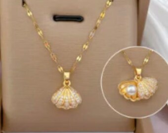 May include: A gold-tone necklace with a pendant shaped like an open seashell with a pearl inside. The shell is decorated with small white stones.