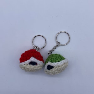 Peut inclure: Deux porte-clés en crochet, l'un rouge et l'autre vert, avec des accents blancs et des yeux noirs. Les porte-clés sont attachés à des anneaux de clés argentés.