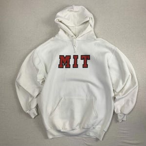 Könnte beinhalten: Weißer Kapuzenpullover mit den Buchstaben "MIT" in roten Blockbuchstaben auf der Brust. Der Pullover hat eine Vordertasche und eine Kapuze mit Kordelzug. Die Ärmel und der untere Saum haben gerippte Bündchen.