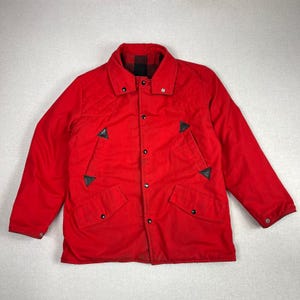 May include: A bright red quilted jacket with a black and red plaid collar. The jacket has black leather accents and two front pockets. It is buttoned up and has a classic, vintage style.