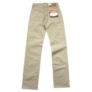 Puede incluir: Vaqueros Levi's 501 de color beige, vistos desde la parte trasera. Los vaqueros tienen un diseño clásico de cinco bolsillos, bragueta con botones y pernera recta. Una etiqueta de Levi's es visible en el bolsillo trasero, junto con una pequeña etiqueta de papel. Los vaqueros son de algodón.