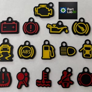 Op de afbeelding: Een verzameling zwarte, gele en rode bedels met waarschuwingslampjes voor het dashboard van een auto. De bedels bevatten symbolen voor de motor, accu, olie, ABS, brandstof en meer. Het Part Lab 3D-logo is ook zichtbaar.