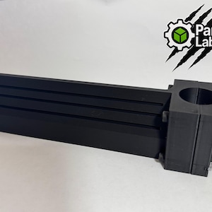 Puede incluir: Componente negro impreso en 3D, con un cuerpo rectangular ranurado y una abrazadera circular. El logotipo "Part Lab3D" es visible. Este elemento probablemente se utiliza en mecánica.