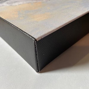 May include: Close-up of the edge of a canvas print with a black frame. The canvas is wrapped around the frame and secured with staples.
