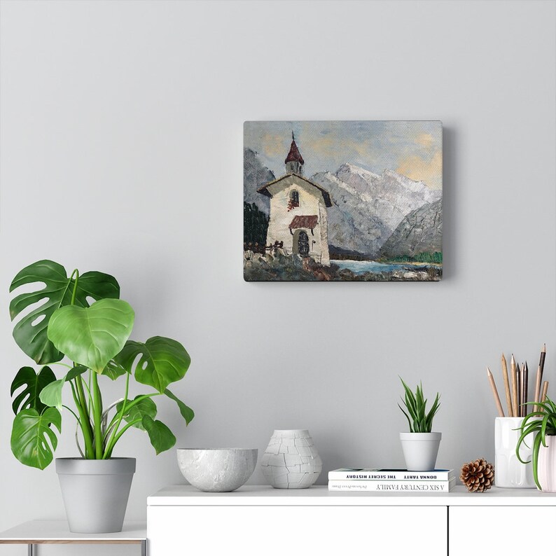 May include: A painting of a white church with a red roof, set against a backdrop of snow-capped mountains and a lake. The sky is a soft blue with hints of gray clouds.