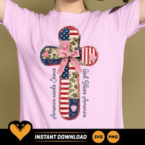 Può includere: Una t-shirt rosa chiaro con una grafica centrale a croce composta da motivi patchwork che includono strisce della bandiera americana, stelle e mimetica. Un fiocco rosa si trova al centro della croce, con il testo America needs Jesus e God Bless America.
