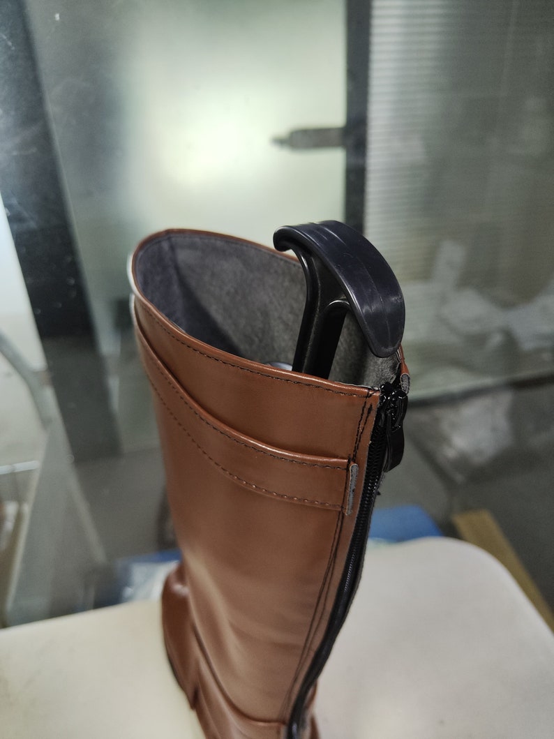 May include: Brown leather knee-high boots with a black zip up the back. The boots have a black plastic boot shaper inside.