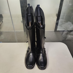 Może przedstawiać: Para czarnych skórzanych kozaków za kolano z klamrami i sznurowadłami.