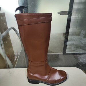 May include: A pair of brown leather knee-high boots with a zip on the inside of the ankle. The boots have a black sole and a buckle on the top of the shaft.