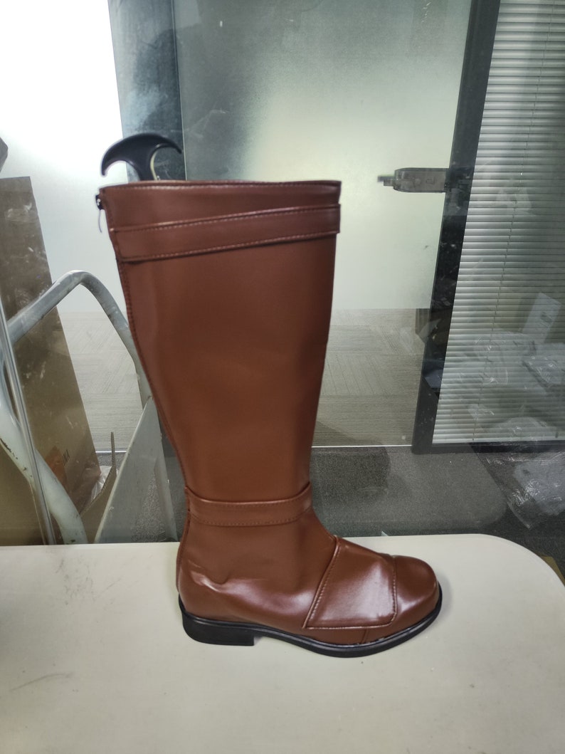 May include: A pair of brown leather knee-high boots with a zip on the inside of the ankle. The boots have a black sole and a buckle on the top of the shaft.